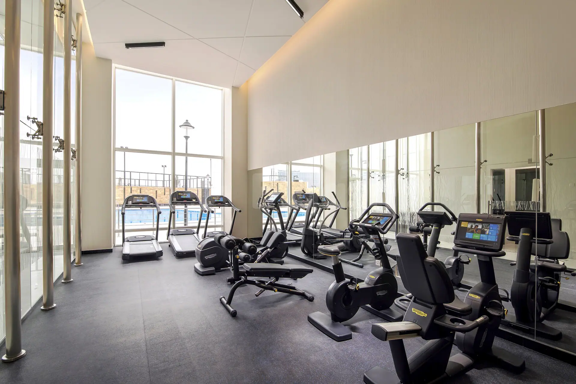 Modern gym at Cristal Amaken Hotel Riyadh featuring treadmills and stationary bikes beside large windows with pool view
