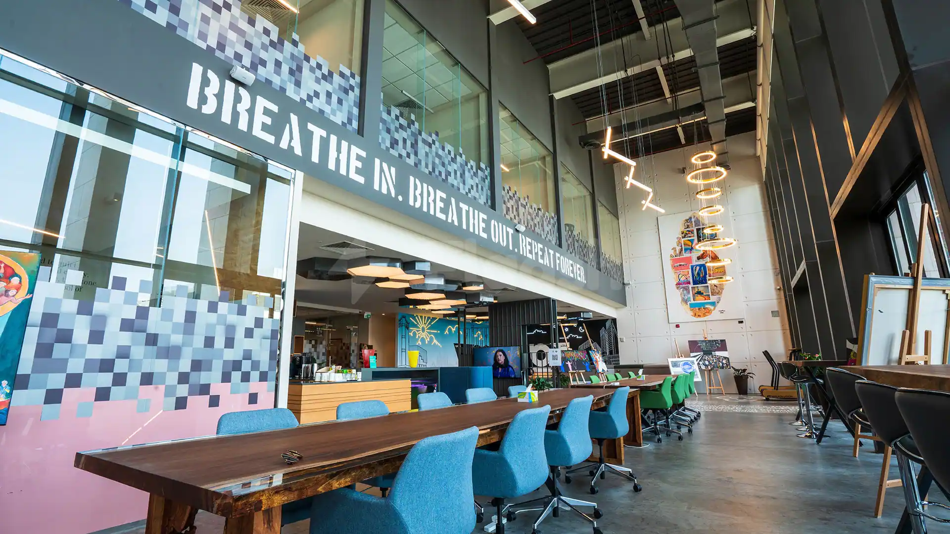 Meeting room at Nestwork Msheireb in Doha featuring a long wooden table, blue chairs, pixelated wall art