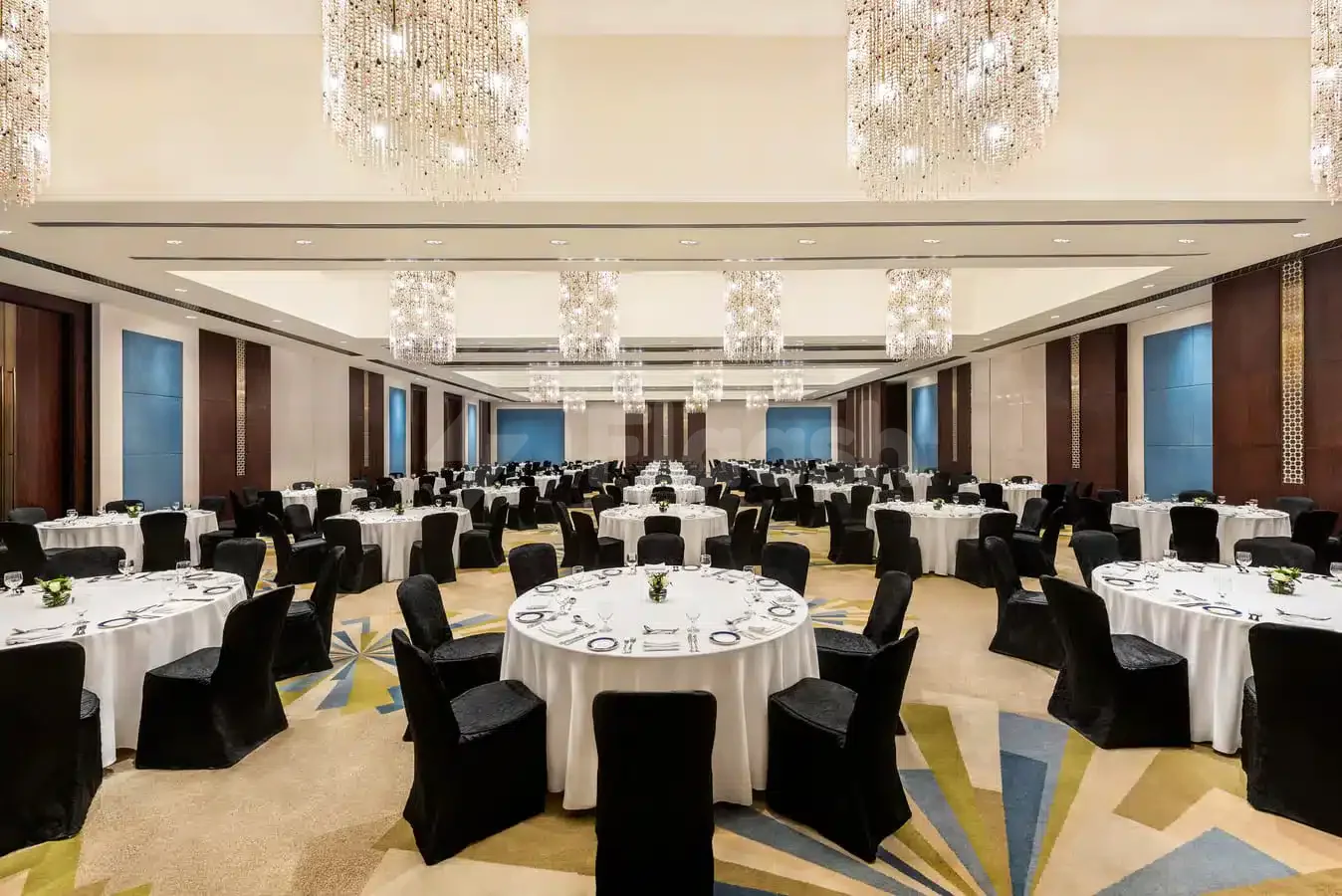 Ballroom at The H Hotel Dubai with round tables set for dining, crystal chandeliers, and geometric patterned carpet