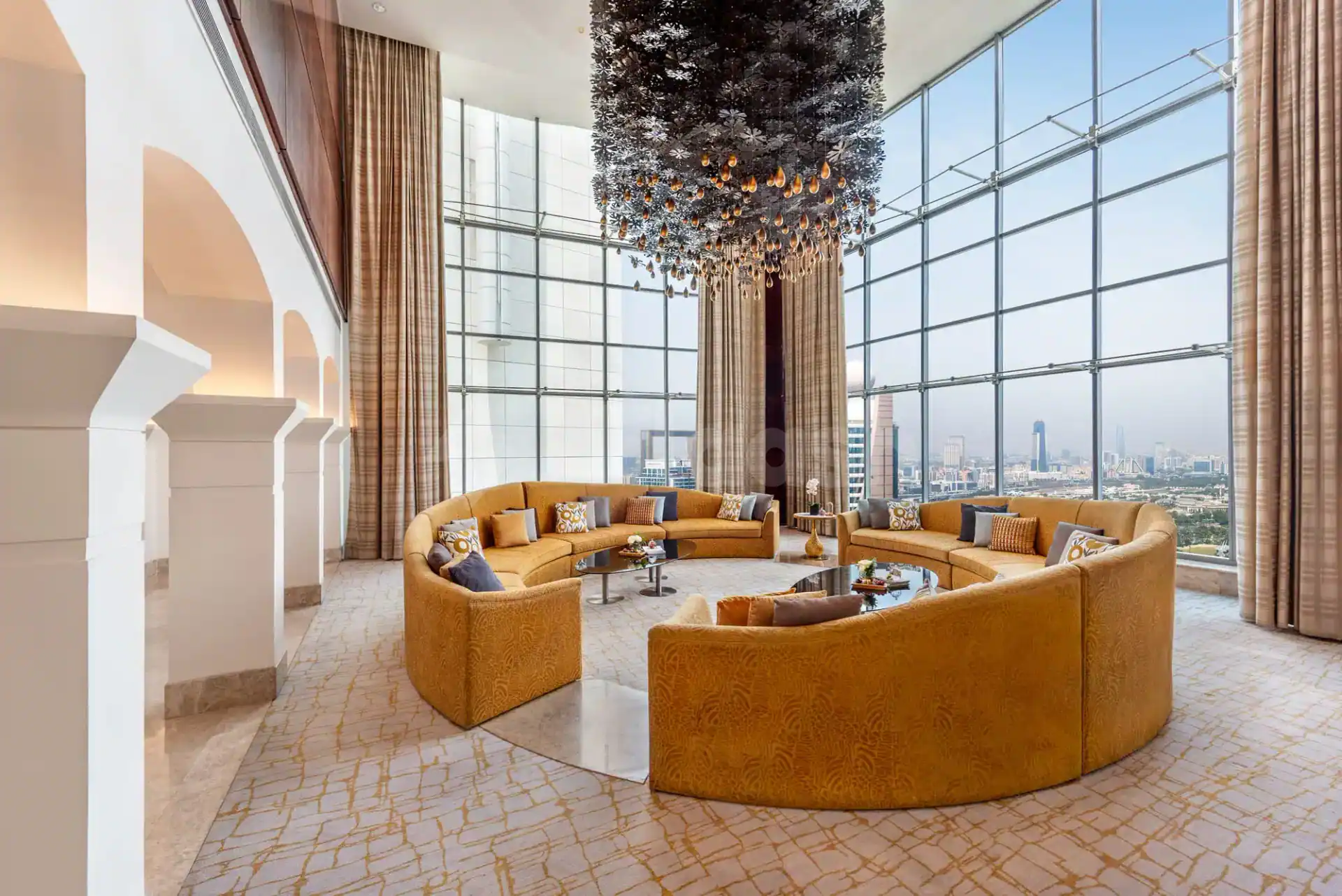 Entrance Hall at The H Hotel Dubai featuring a curved mustard-yellow sofa and large floor-to-ceiling windows