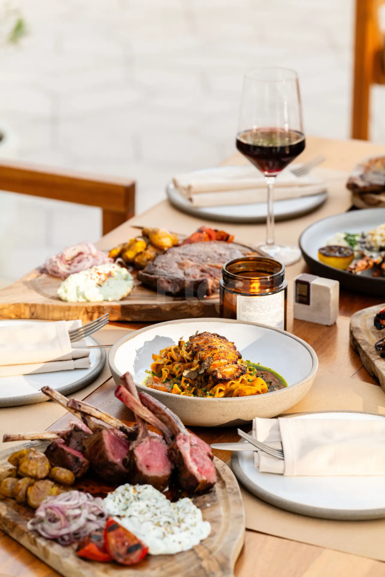 Restaurant table at Ergon Deli & Cafe Abu Dhabi with grilled lamb chops, pasta, and red wine in natural