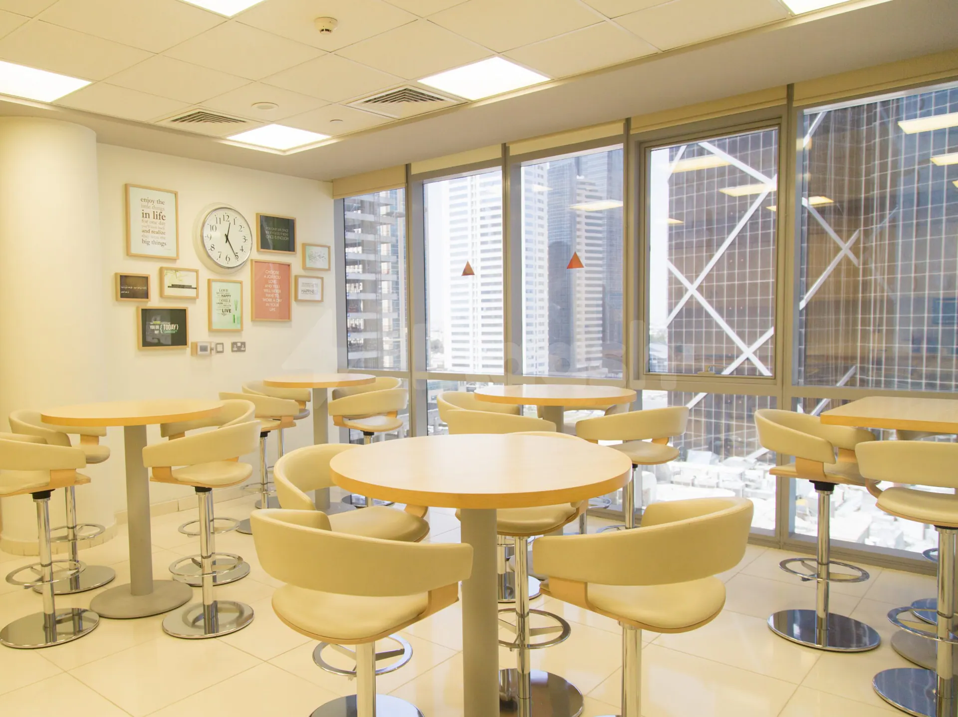 Restaurant at Globex Business Centre Doha featuring round wooden tables, cream bar stools, and large windows with city