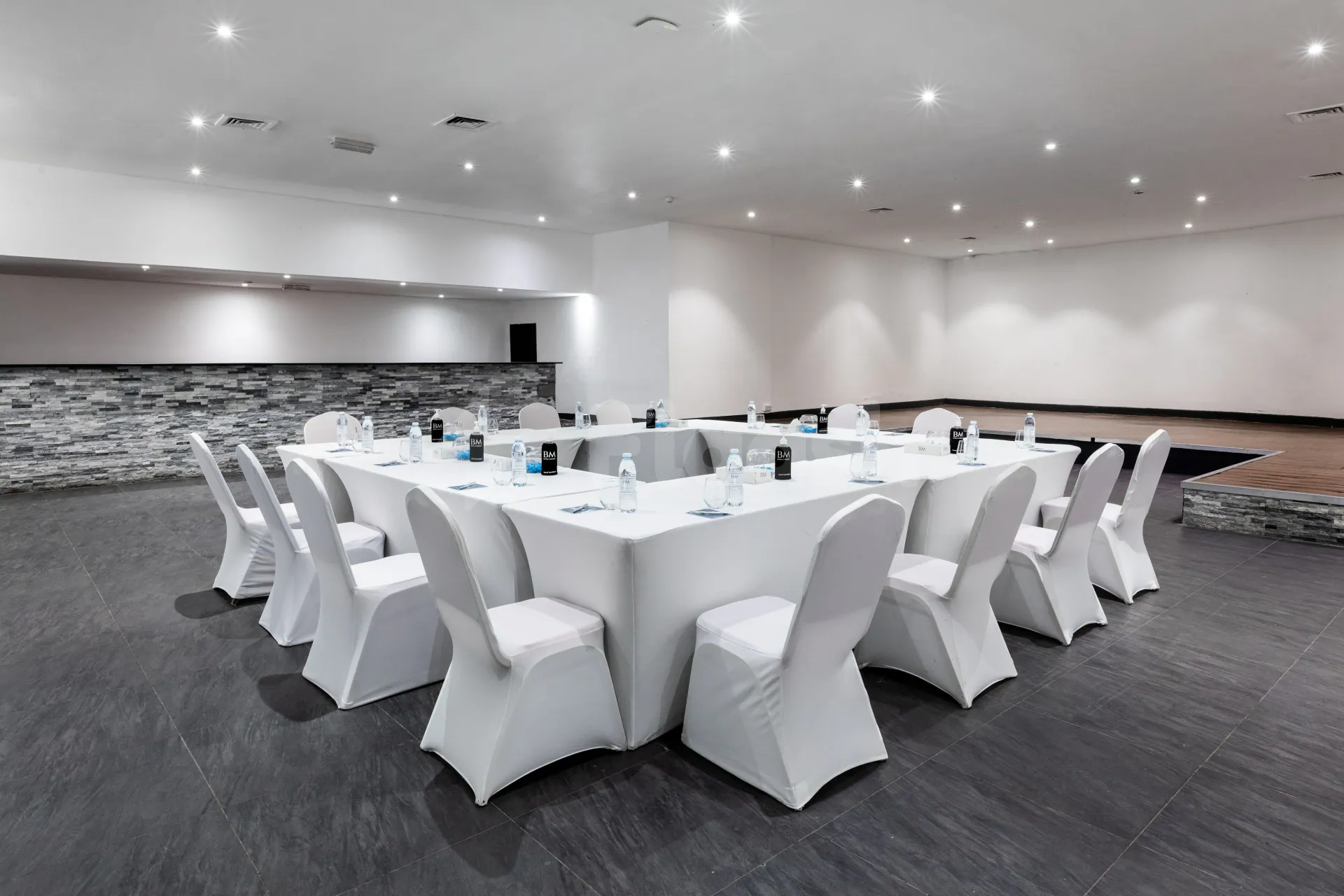 Meeting room at Bm Beach Resort Ras Al Khaimah with white-covered tables and chairs, stone accent wall
