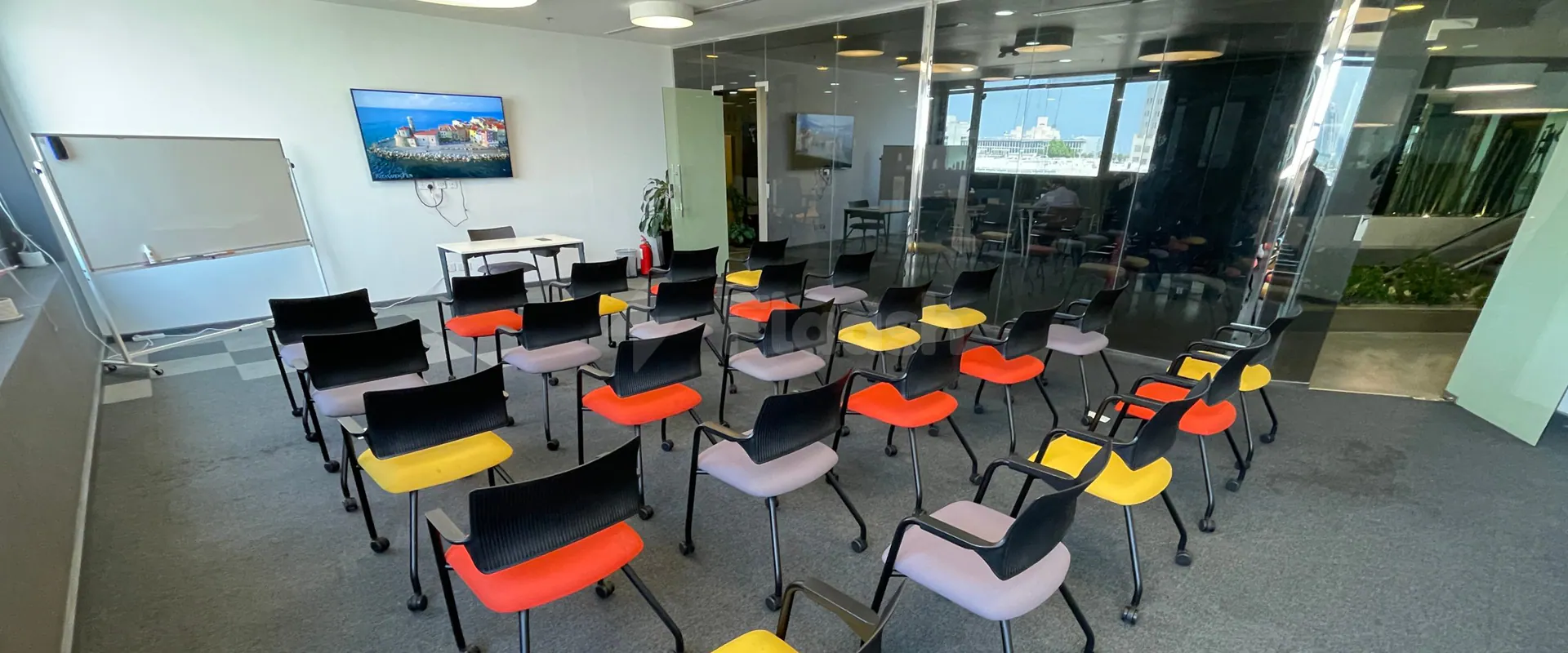 Meeting room at Nestwork Msheireb in Doha with arranged chairs, a whiteboard on stand, and a mounted TV