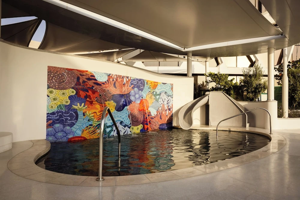 Indoor pool at Rosewood Doha, Lusail, featuring vibrant coral mosaic wall and white slide under modern canopy