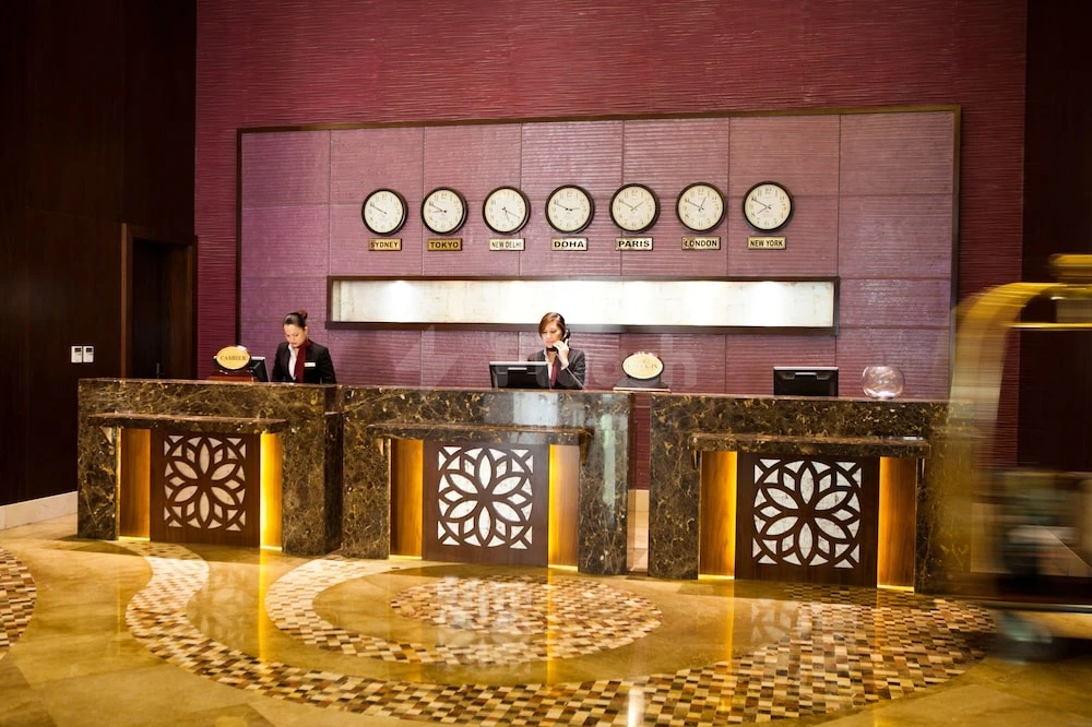 Lobby at Grand Regal Hotel, Doha, featuring marble counters and illuminated world time clocks on a burgundy wall