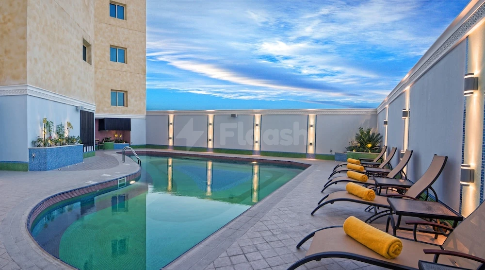 Rooftop pool at Grand Regal Hotel, Doha, with yellow towels on loungers under a twilight sky