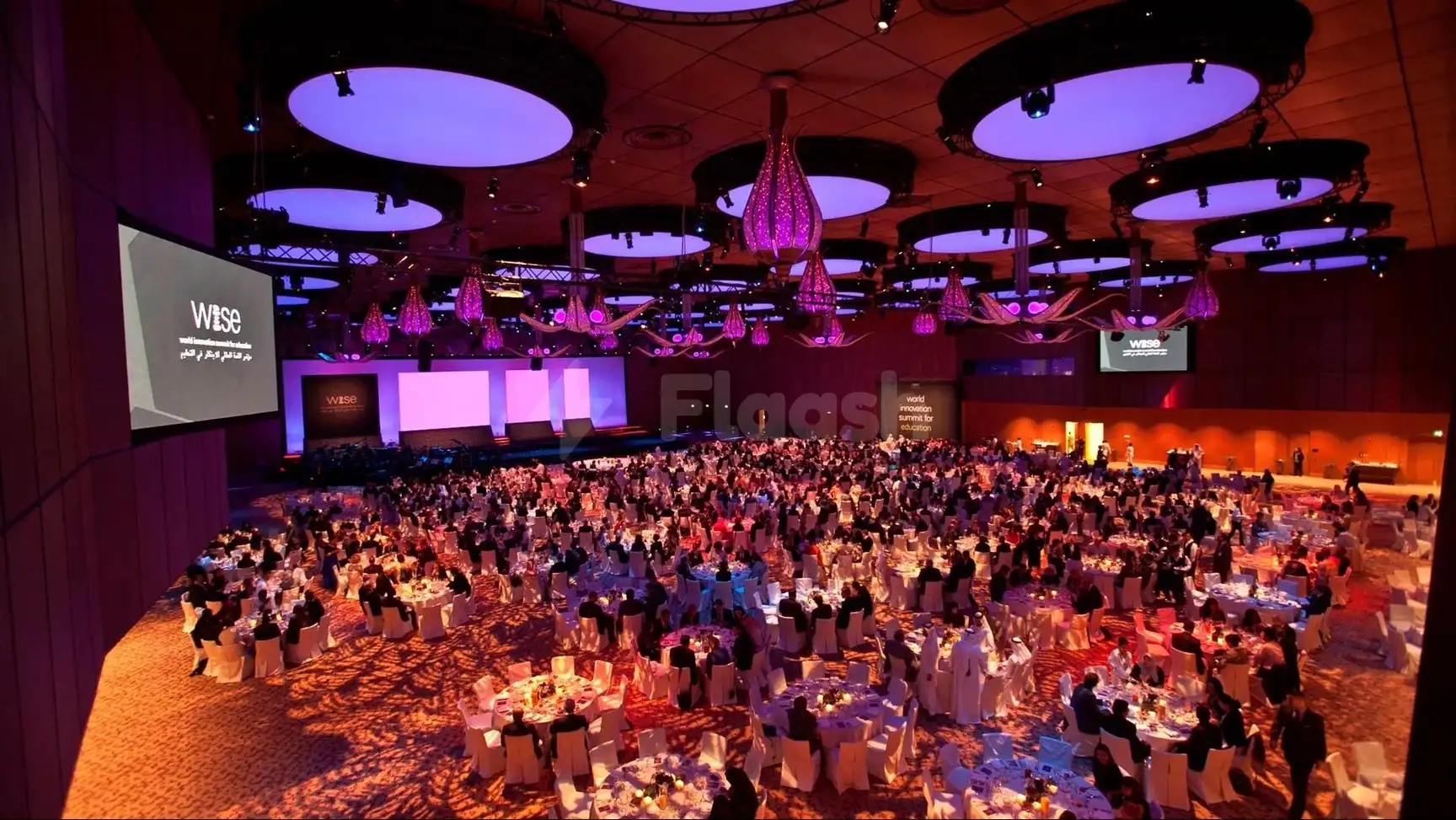 Grand ballroom at Qatar National Convention Centre, Doha, with circular tables under purple-lit ceilings and a central stage
