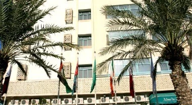 Facade of Al-Muntazah Plaza Hotel in Doha framed by palm trees and colorful flags along the building’s lower