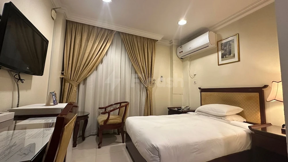 Guest room at Al-Muntazah Plaza Hotel, Diba, featuring bed with white linens, wooden furniture, and wall-mounted TV