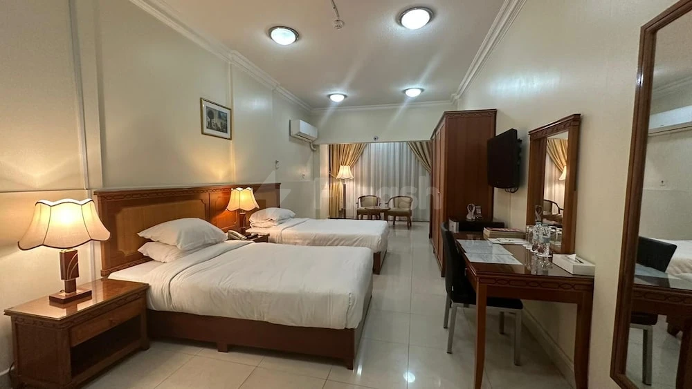 Guest room at Al-Muntazar Plaza Hotel, Doha, featuring twin beds with wooden headboards and bedside lamps