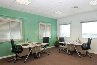 Workspace at Regus Doha Airport, Doha, featuring mint green walls and multiple desks under bright ceiling lights