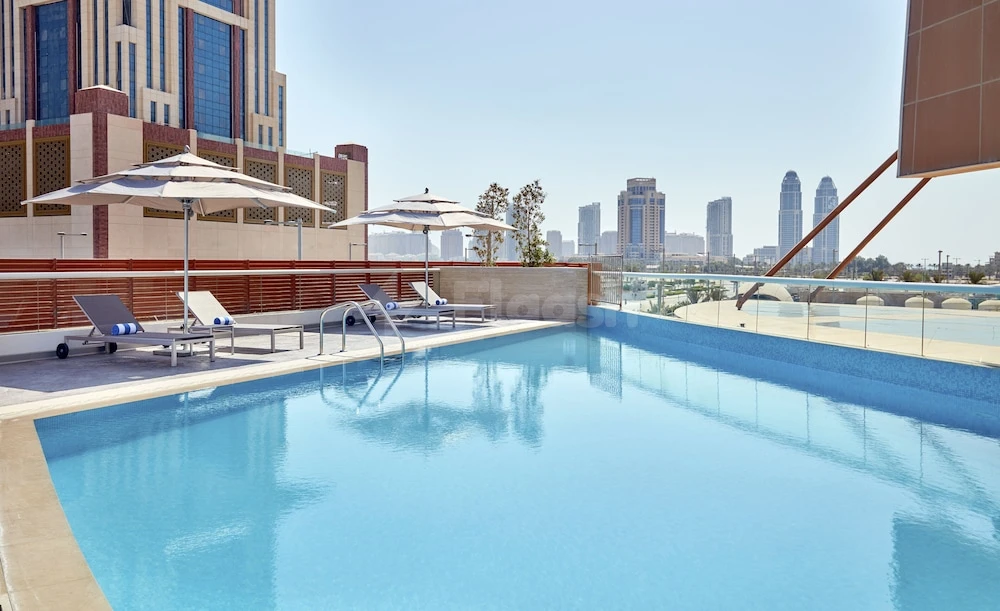 Rooftop pool at Staybridge Suites Doha Lusail, Lusail, with city skyline and lounge chairs under umbrellas