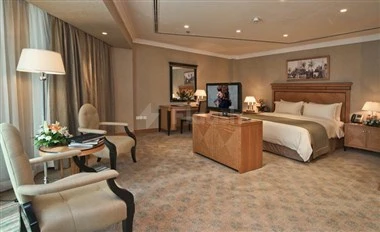 Luxury guest room at Retaj Royale Doha, featuring plush seating and a large bed with wooden headboard