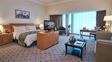 Luxury hotel room at Retaj Royale Doha, Doha, featuring a large bed, flat-screen TV, and expansive window view