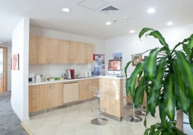 Modern kitchenette at Regus - Doha West Bay, Doha, featuring wooden cabinetry and a bar stool beside lush greenery