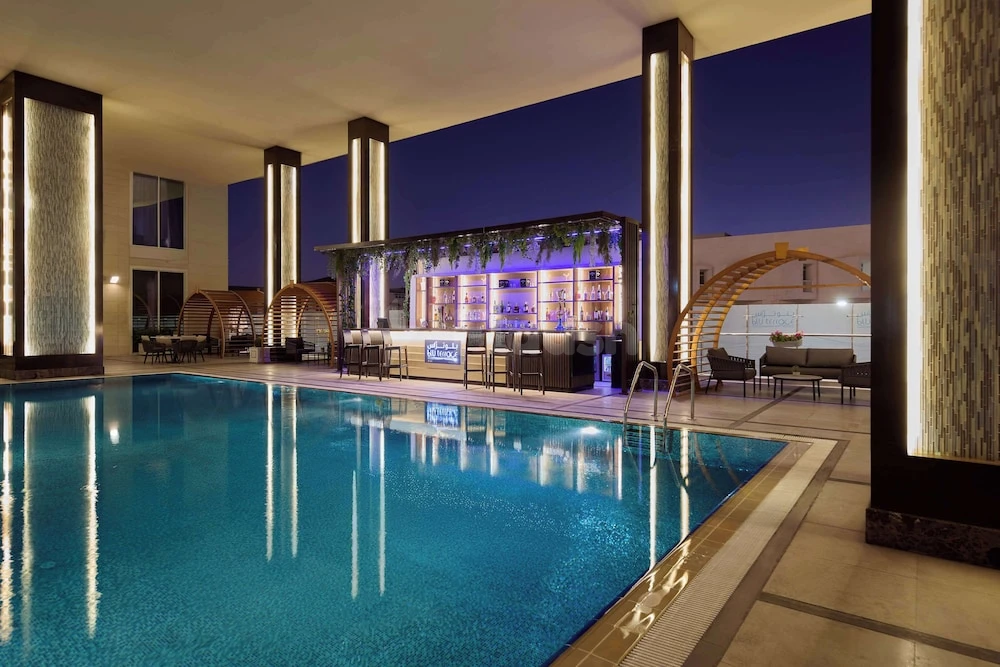 Indoor pool at DoubleTree by Hilton Doha - Al Sadd, Doha, featuring illuminated columns and a purple-lit bar