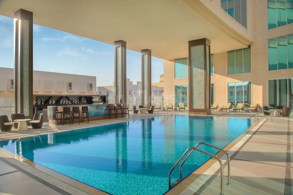 Outdoor pool at DoubleTree by Hilton Doha - Al Sadd, Doha, featuring a bar area and glass-walled columns under
