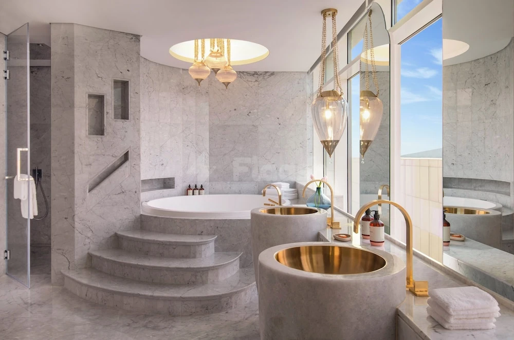 Marble bathroom at Abesq Doha Hotel & Residences, Doha, featuring gold sinks and a sunken bathtub with steps
