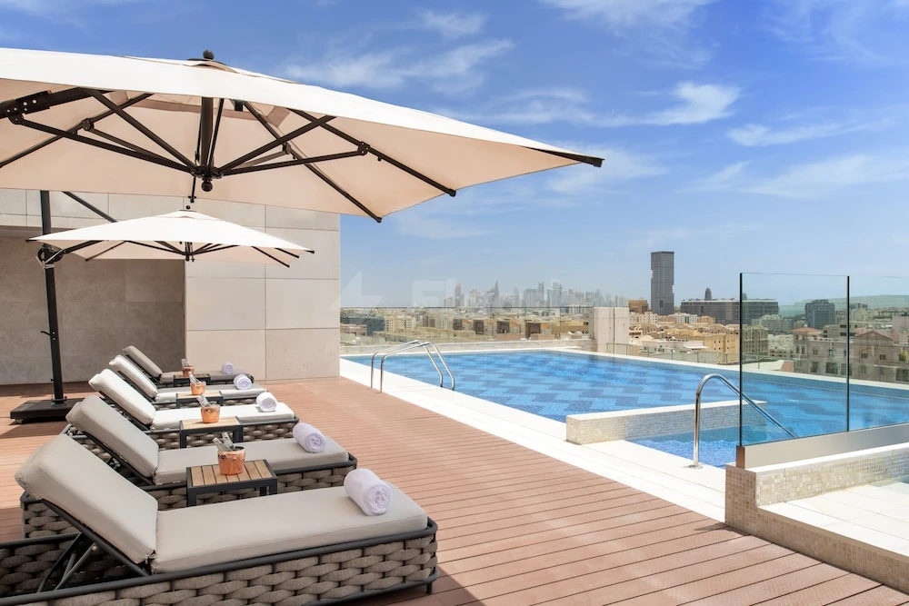 Rooftop pool at Abesq Doha Hotel & Residences, Doha, with city skyline view and lounge chairs under umbrellas