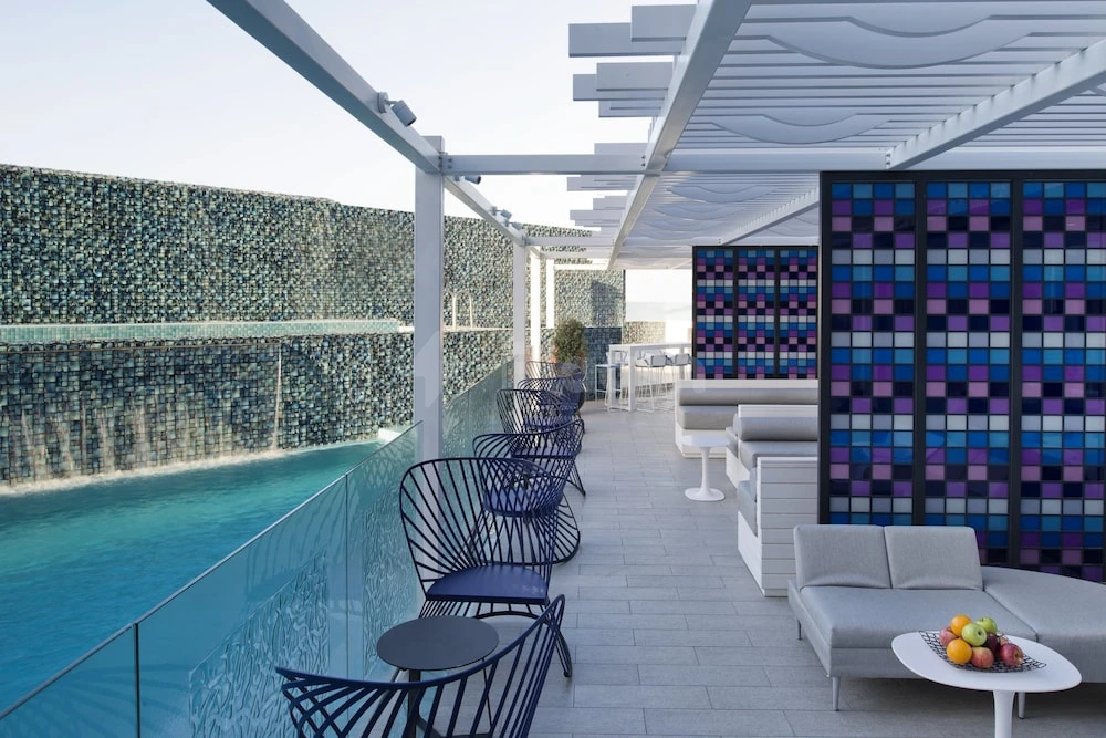 Outdoor lounge area at W Doha, Doha, featuring blue mosaic wall art beside turquoise pool