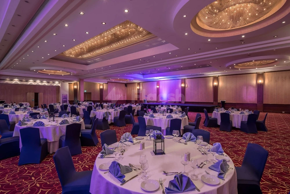 Banquet hall at Radisson Blu Hotel, Doha, with round tables set under a grand chandelier and purple ambient