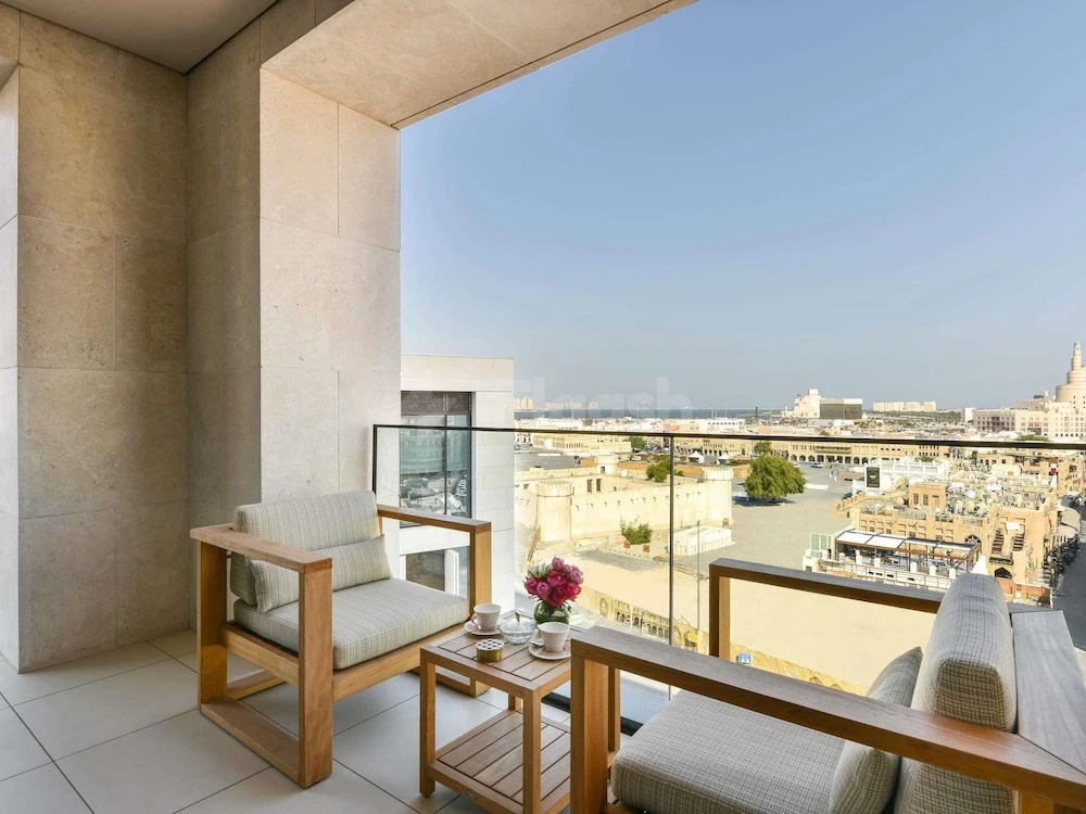 Balcony at Alwadi Hotel Doha MGallery By AccorHotels, Doha, with wooden furniture and city view under clear sky