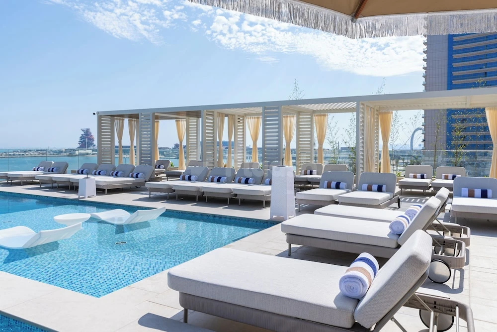Poolside lounge area at The OQ Hotel, Lusail, with white sunbeds and blue-tiled water feature