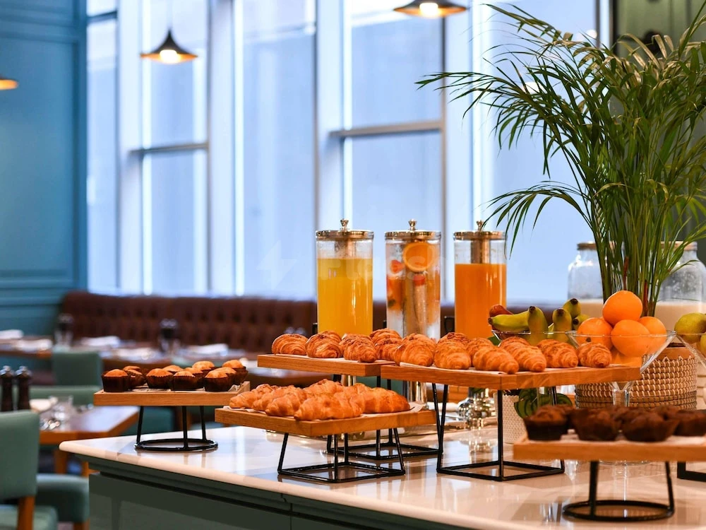 Breakfast buffet at Adagio Doha, Doha, featuring croissants pastries and citrus drinks on tiered stands near large windows