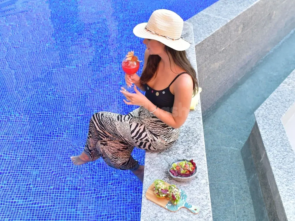 Poolside lounge at Adagio Doha, Doha, with woman sipping cocktail by blue mosaic pool edge