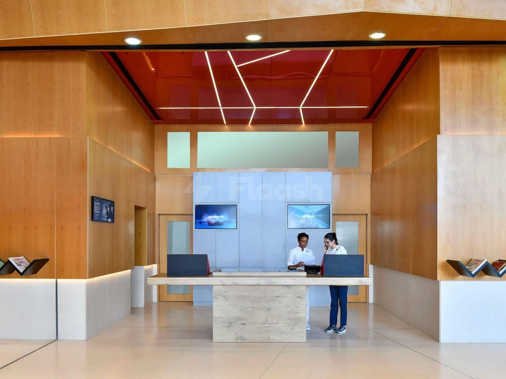 Reception area at Adagio Doha, Doha, featuring warm wood panels and a red geometric ceiling with embedded lighting