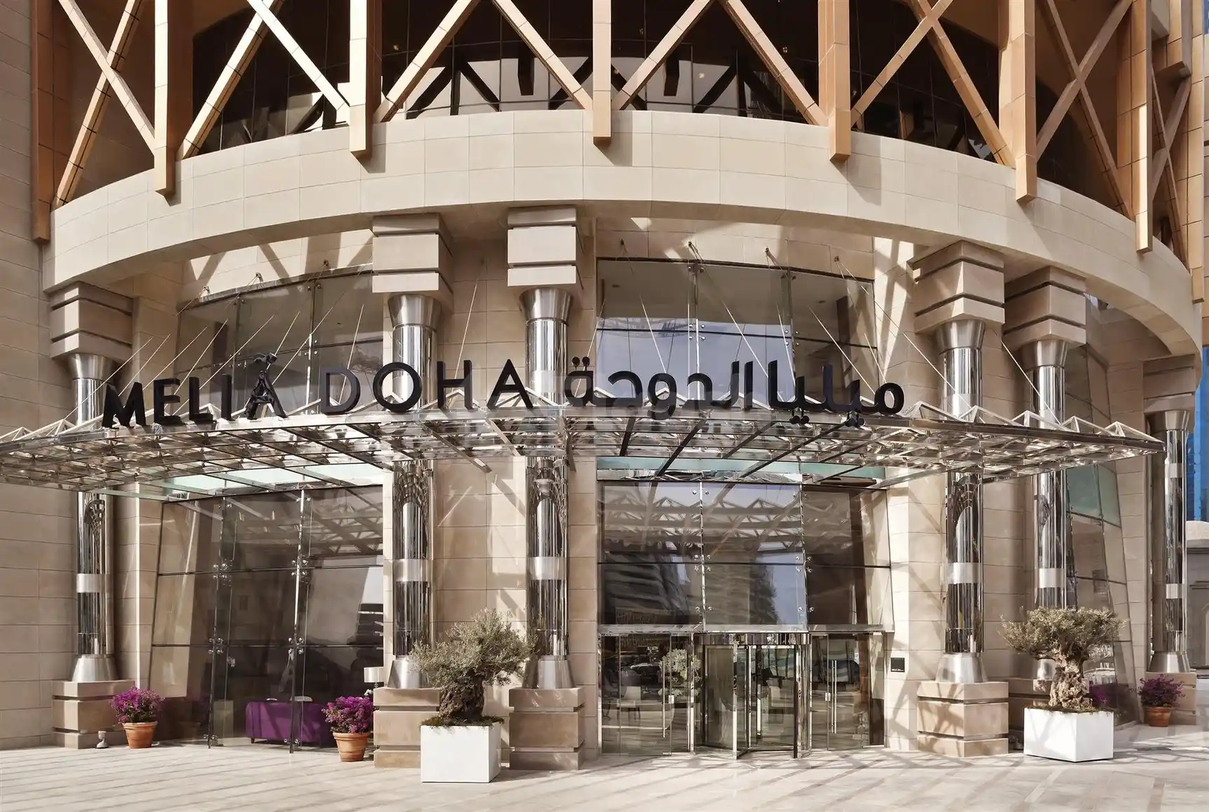 Grand entrance at Melia Doha, Doha, featuring glass canopy and stone pillars with Arabic script signage