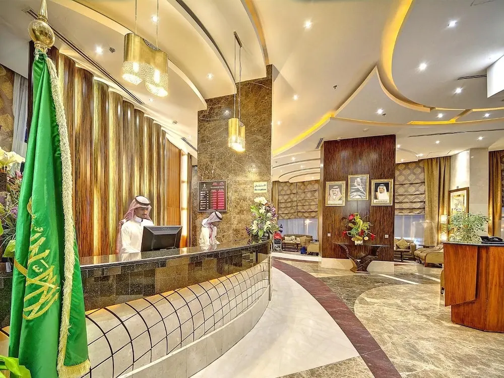 Lobby at Elaf Kinda Hotel, Mecca, featuring a green Saudi flag and marble reception desk under modern ceiling