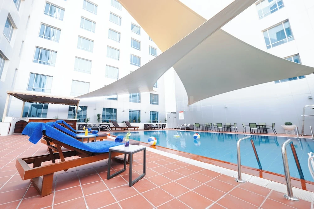 Outdoor pool area at ibis Jeddah City Center, Jeddah, featuring shaded loungers and large white canopy sails
