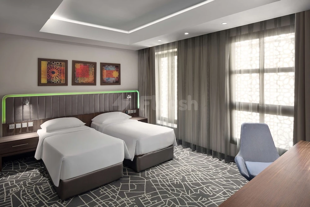 Guest room at Park Inn by Radisson Makkah Aziziyah, featuring twin beds, geometric carpet, and framed abstract art