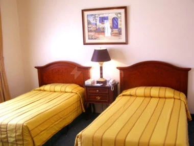 Guest room at Sunset Jeddah, Jeddah, featuring twin beds with yellow striped linens and framed artwork above nightstand