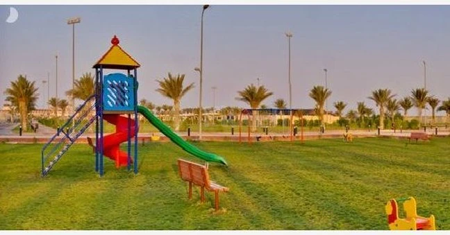 Playground equipment at Boudl Half Moon Resort, Khobar, featuring a colorful slide and climbing frame on green grass