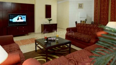 Living room at Boudl Al-Corniche, Dammam, featuring red patterned sofas and a TV mounted on dark wood cabinetry