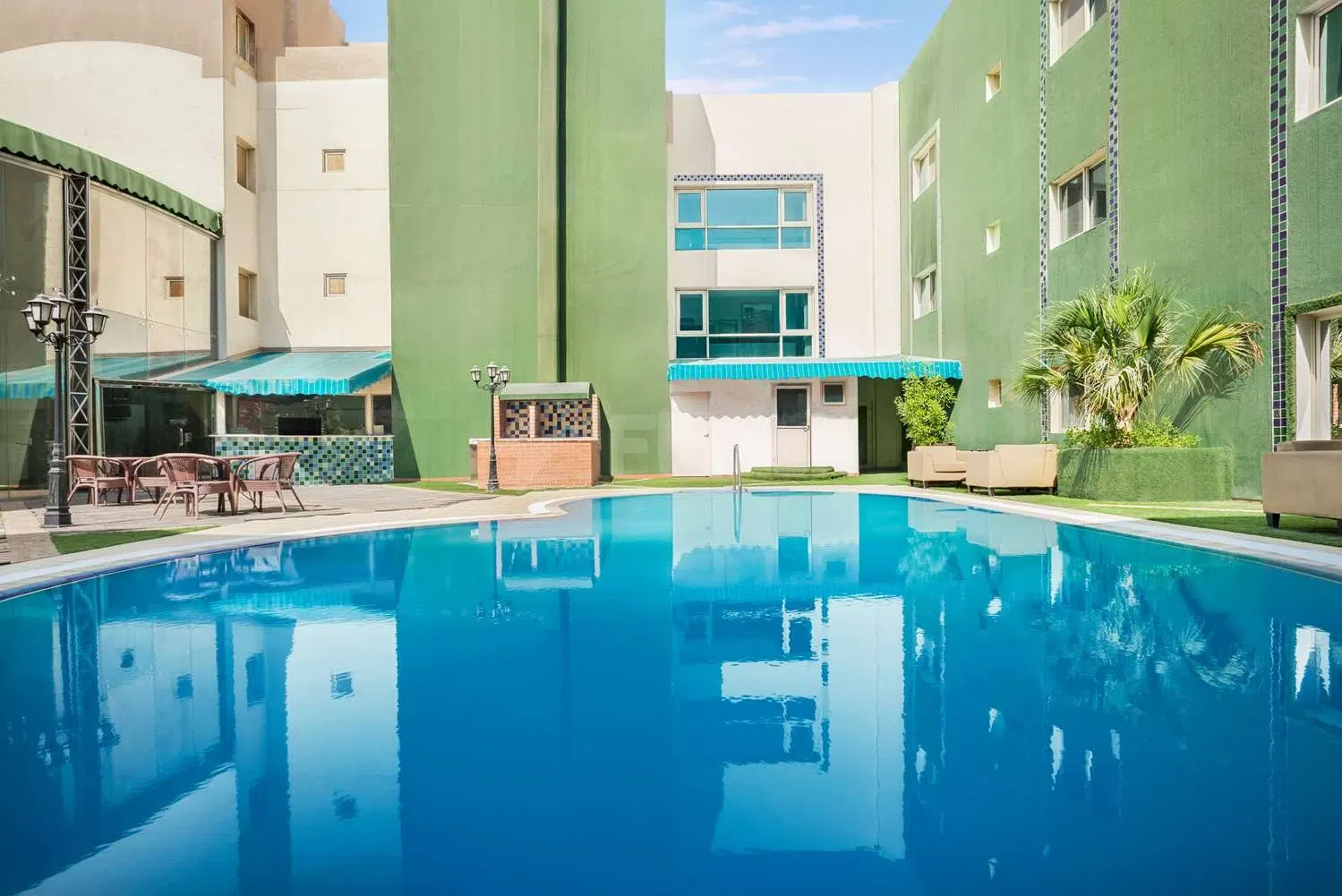 Outdoor swimming pool at Ramada by Wyndham Dammam Khaleej Road, Dammam, surrounded by green walls and turquoise awnings
