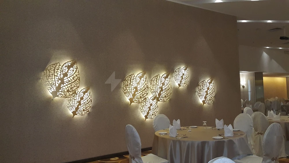 Banquet hall at M Hotel Makkah By Millennium, Mecca, featuring illuminated leaf wall art and round tables