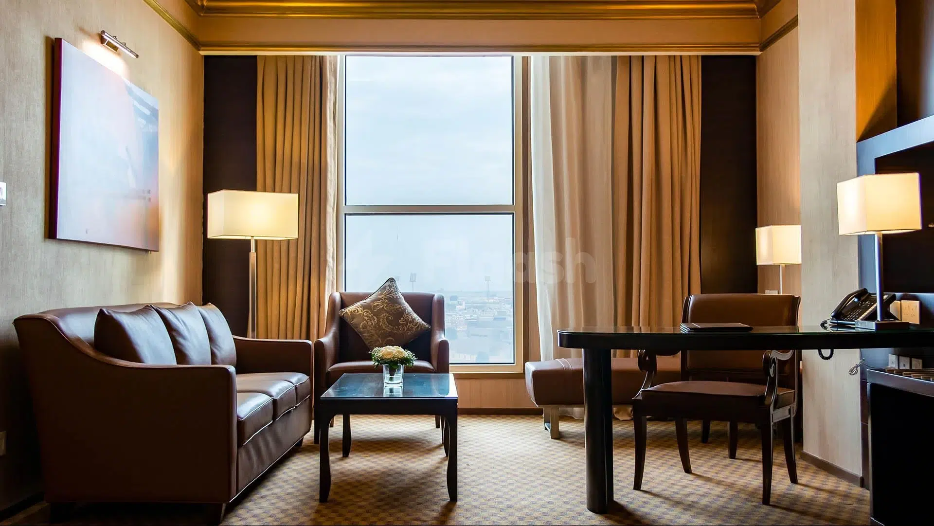 Lounge area at Wyndham Garden Dammam, Dammam, featuring leather sofa, coffee table, and city view through large window
