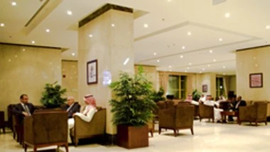 Lobby at Makarim Al-Bit Hotel, Mecca, with potted plants and guests in traditional attire seated on brown armchairs