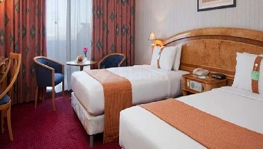 Guest room at Gloria Inn Naj! Najran, with wooden headboard and patterned curtains, red carpeting, and side chairs