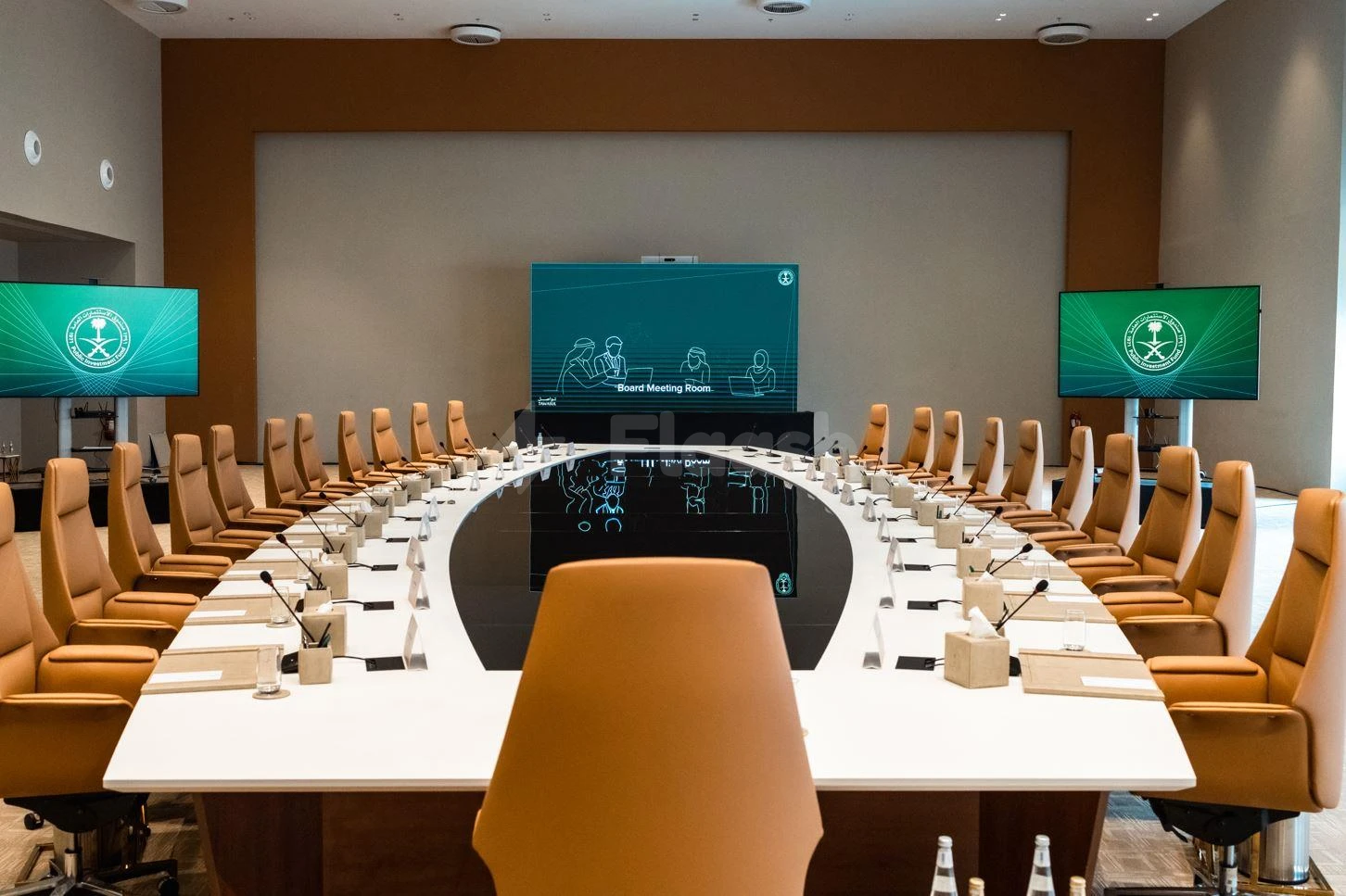 Boardroom at Maraya, AlUla, with three large digital screens and tan leather chairs arranged around a white oval