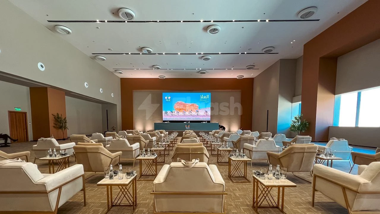 Conference hall at Maraya, AlUla, featuring tiered beige seating and a large screen displaying Arabic content against warm-toned