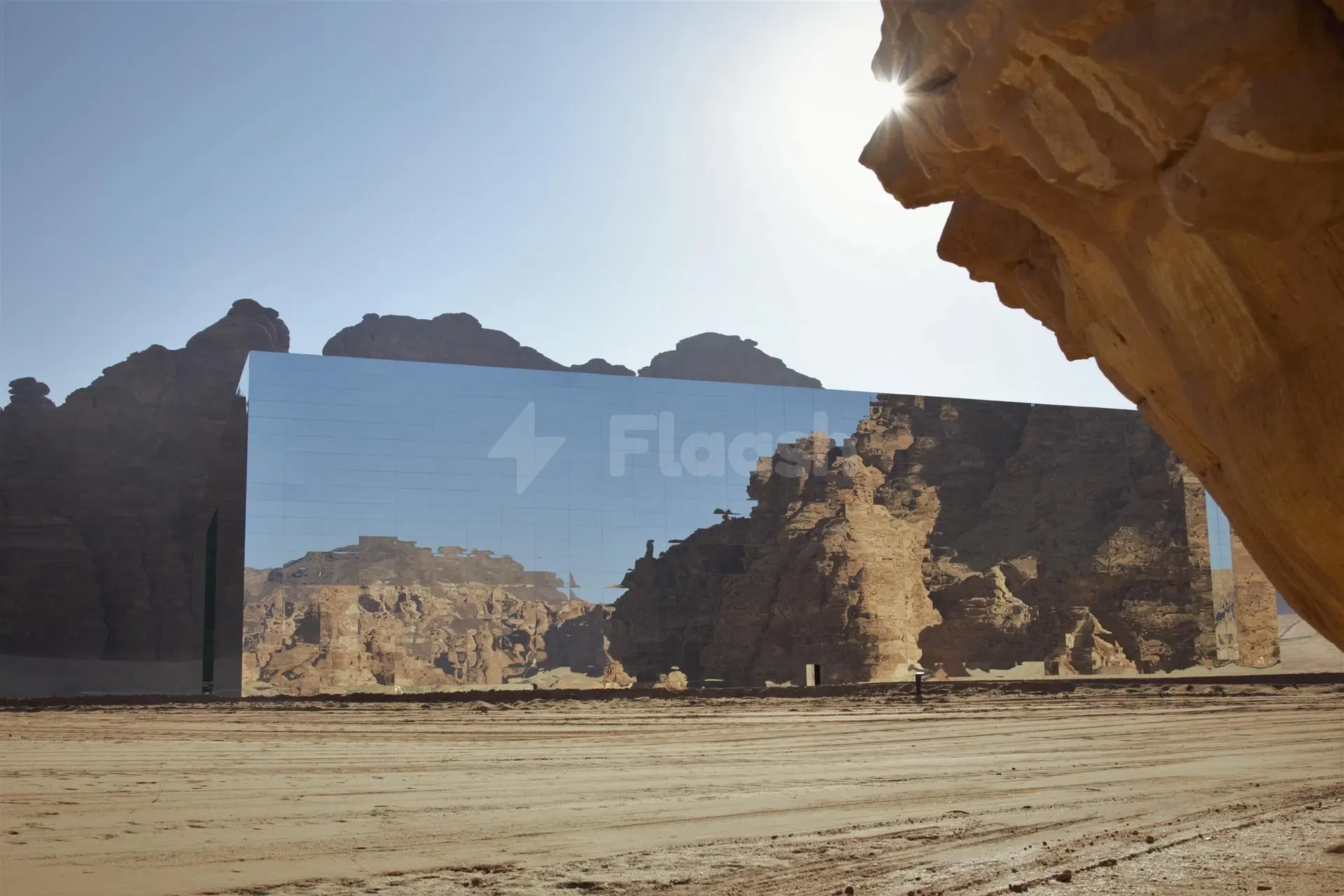 Mirror-clad concert hall at Maraya, AlUla, reflecting desert cliffs under bright sun from rocky overhang