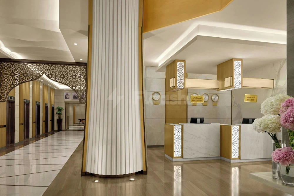 Lobby at Sheraton, Makkah, featuring marble reception desks with illuminated geometric insets and a tall fluted column