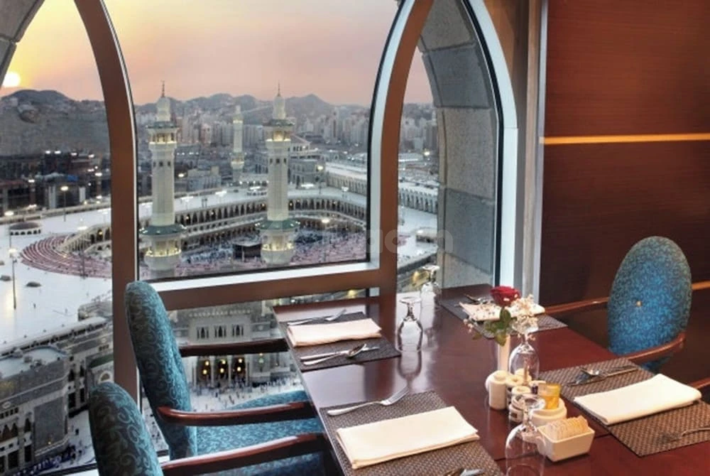 Dining table at Al Marwa Rayhaan by Rotana - Makkah, with arched window view of Masjid al-Haram and city