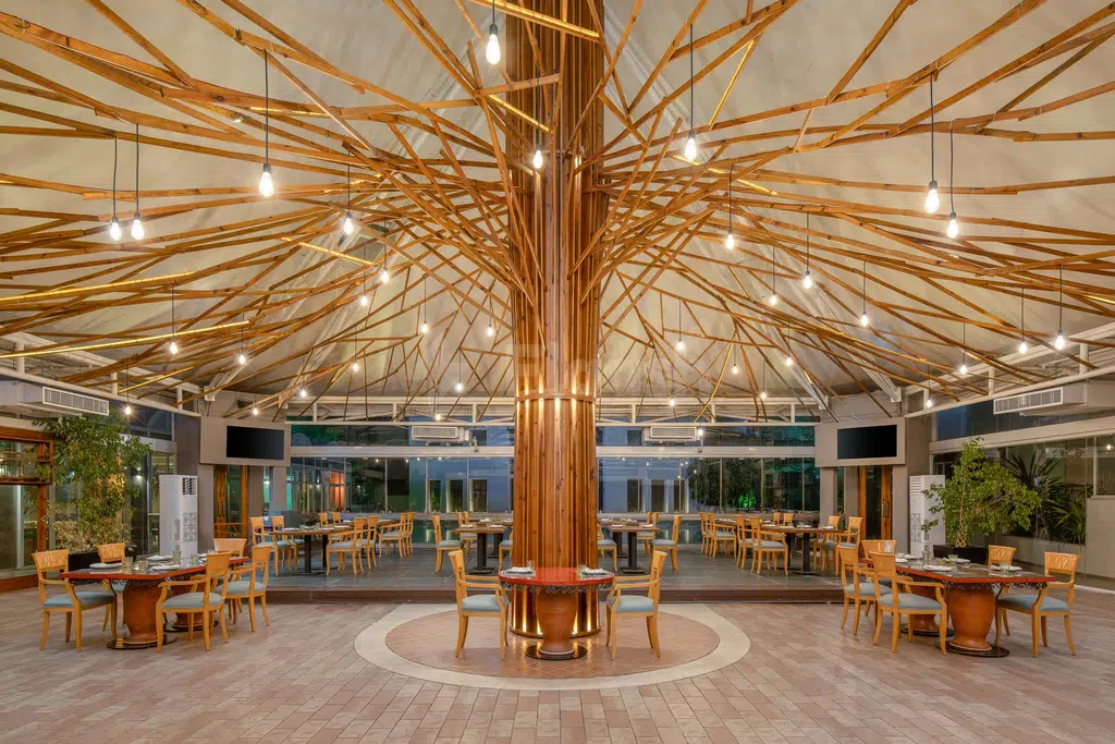 Dining area at Carlton Al Moaibed Hotel, Dammam, featuring central wooden pillar and suspended lights over terracotta tables