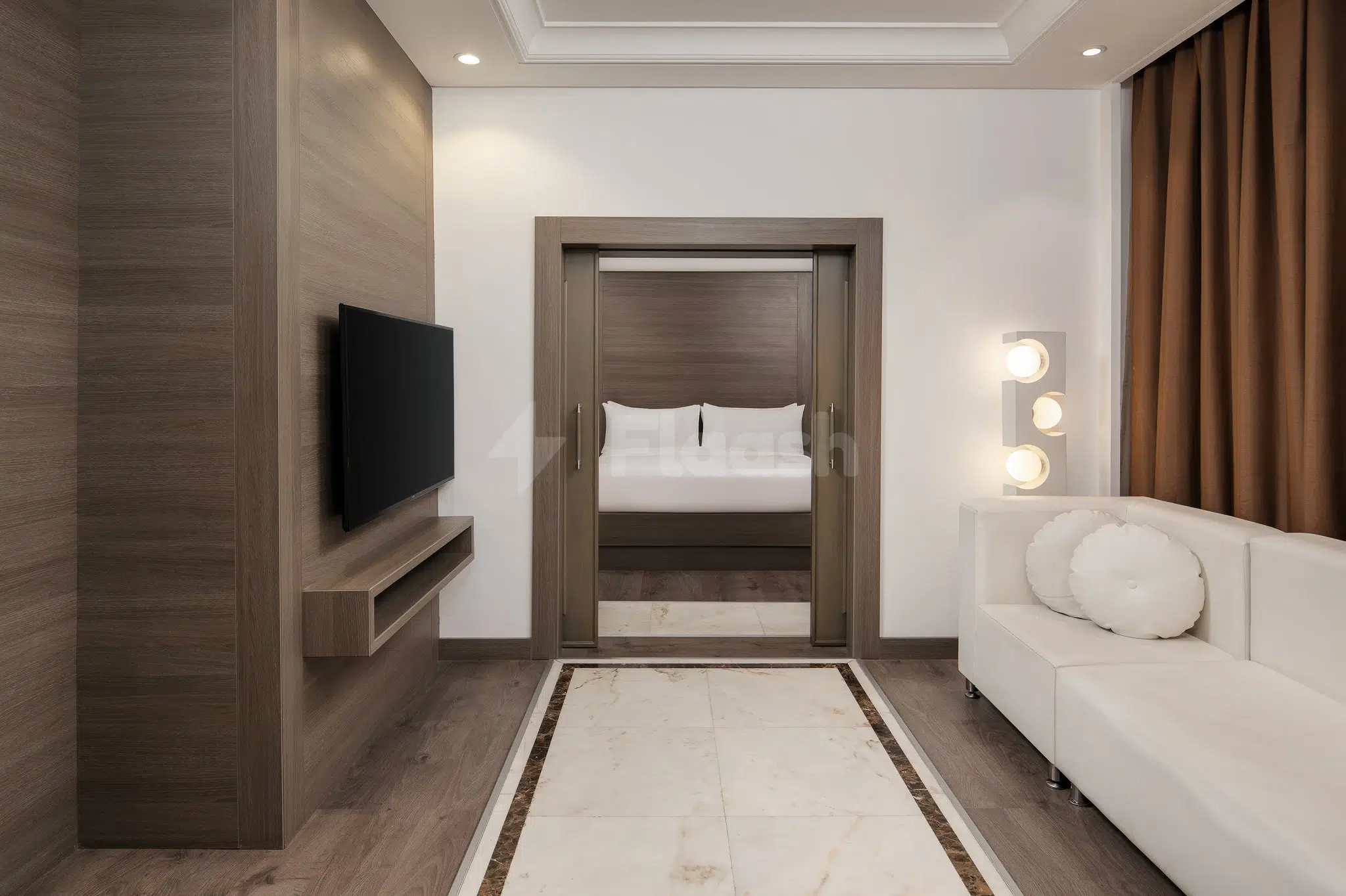 Guest room at Carlton Al Moaibed Hotel, Dammam, featuring wood-paneled walls, a white sofa, and a bed visible